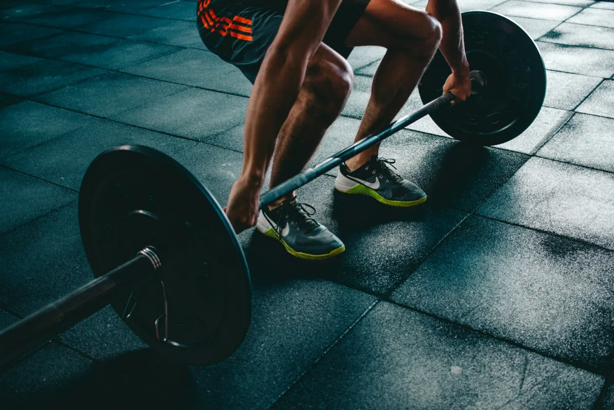 Athlete in running shoes gripping a loaded barbell for a deadlift