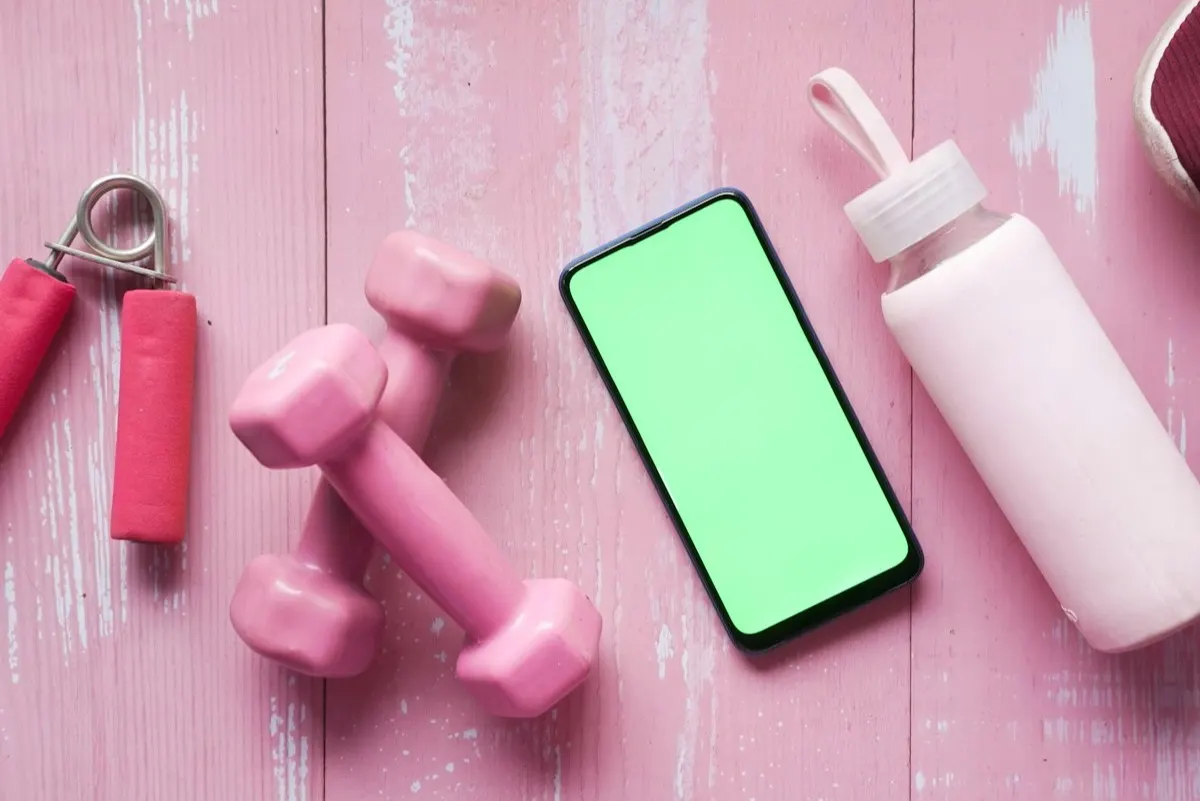 A fitness app open on a smartphone beside workout gear and a water bottle