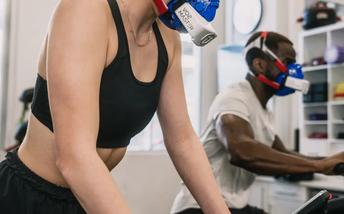 Two athletes performing a VO2 max test on cycle ergometers with gas exchange masks in a fitness lab